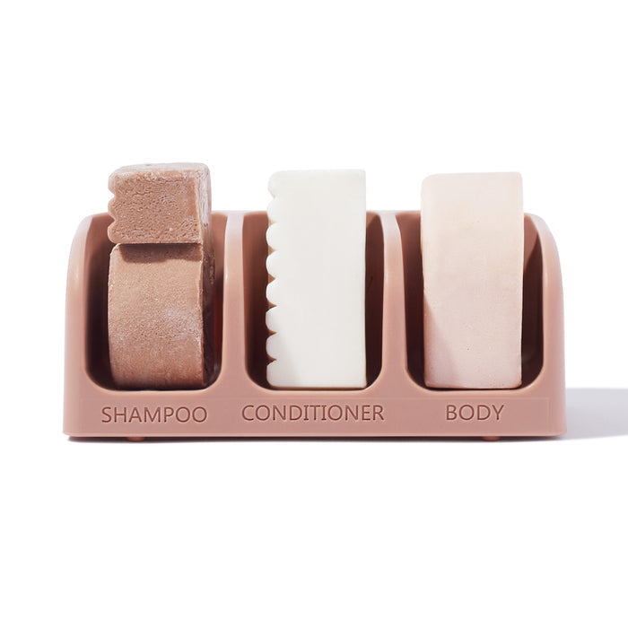 Kitschs Self Draining Soap Dish set for Bottle-Free Beauty includes a textured brown shampoo bar, a white comb-like conditioner bar, and a smooth beige body bar, each with its own compartment.