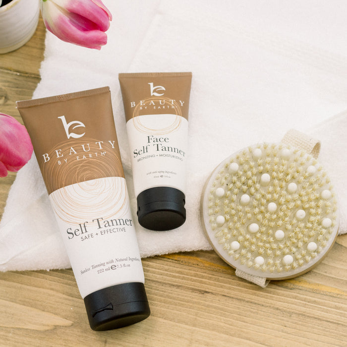 Beauty by Earths Self Tanner and face self tanner promise a sun-kissed glow, showcased with a textured brush, white towel, and pink tulips on a wooden surface.