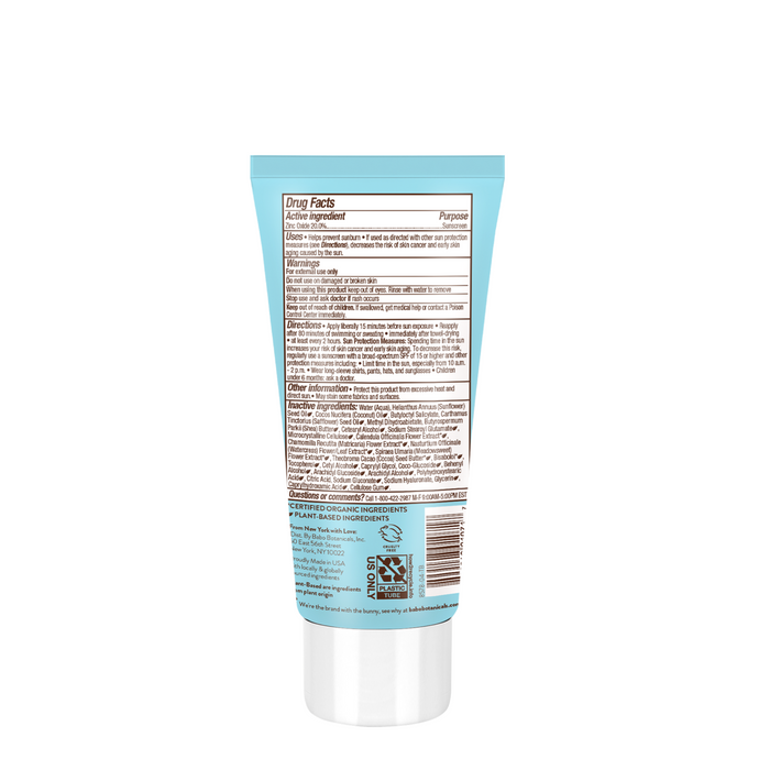 A light blue tube with a white cap, shown from the back, displays black text listing drug facts and directions. This is Babo Botanicals Sensitive Baby Mineral Sunscreen Lotion SPF50; the broad spectrum product info appears detailed but not fully legible.