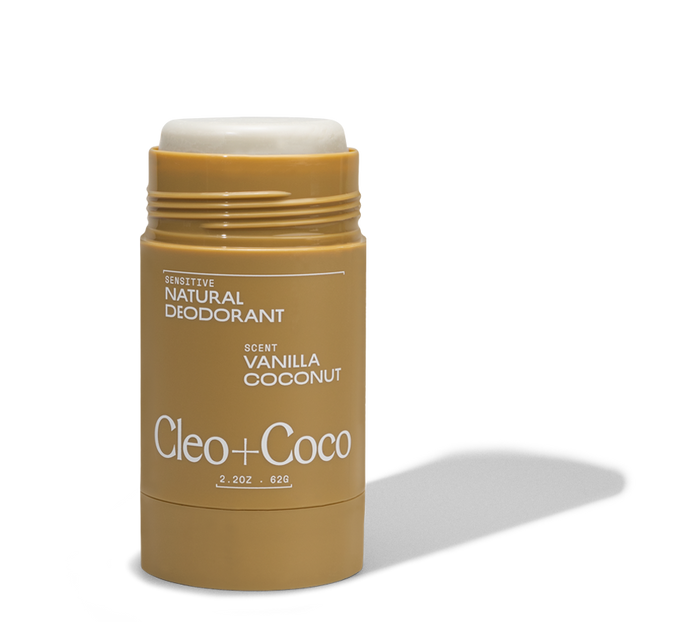 A tan stick of Cleo & Coco Sensitive Deodorant in Vanilla Coconut scent with the cap off, showing the deodorant inside. The label highlights odor control and features activated charcoal for added freshness.