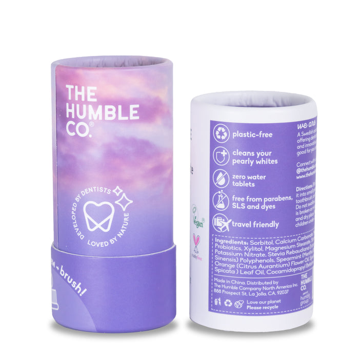 Two purple tubes from The Humble Co. are displayed. The front features the brand, while the back highlights plastic-free and ingredients. These Sensitive Toothpaste Tabs come in eco-friendly packaging and are fluoride-free, with a white toothbrush logo.