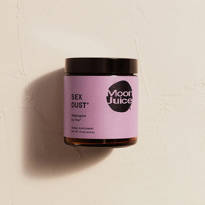 A jar of Moon Juice Sex Dust on a white background features a purple label with black text, highlighting its adaptogenic benefits for libido, hormonal balance, and creative energy. It is sealed with a sleek black lid.