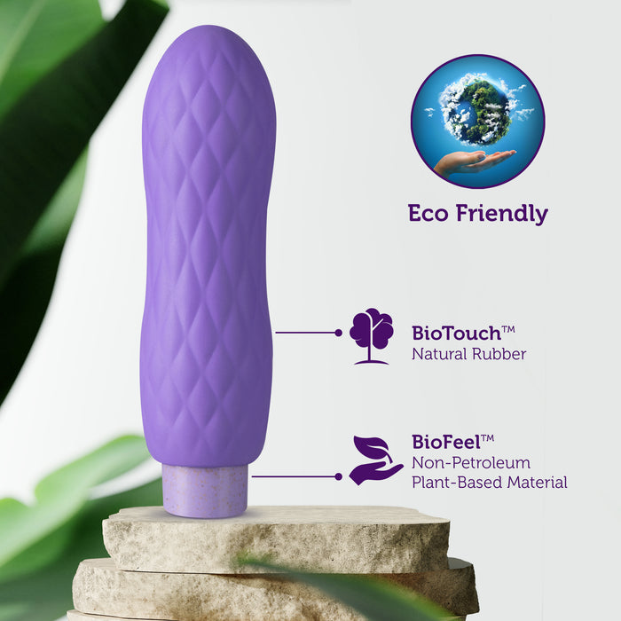 A purple, textured object stands on stacked stones surrounded by plants. Text highlights its eco-friendly design, featuring BioTouch™ natural rubber and BioFeel™ non-petroleum plant-based materials. A globe in a hand symbolizes sustainability.