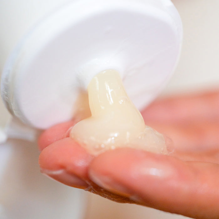 A hand presses a white Wildcraft Shampoo pump bottle, dispensing a creamy, translucent quinoa protein-infused gel onto the fingers. The shiny gel suggests moisturizing or cleansing properties against a blurred, neutral background.