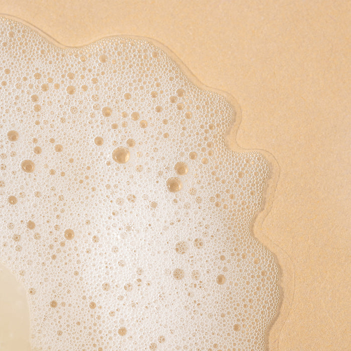 Close-up of frothy bubbles on the beige surface of Wildcraft Shampoo, creating an abstract pattern with smooth, wavy edges against a solid backdrop.