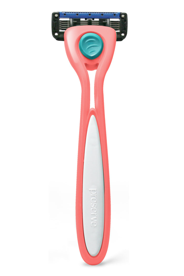 A pink and white Preserve Shave 5 razor with ceramic-coated blades and a blue cover sits upright on a white background. The recycled plastic handle features a turquoise grip near the blade, with Preserve Shave 5 embossed on it.