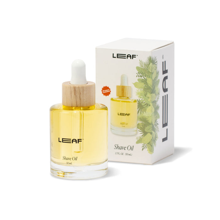 A glass bottle of Shave Oil w/ Dropper featuring a wooden lid sits before a box emblazoned with Leaf Shave, displaying the moisturizing shave oil beside green leaves, promising to soothe irritation and enhance your shaving experience.