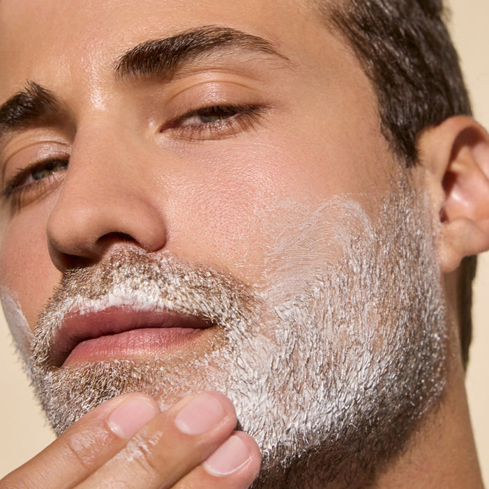 A man applies Phil's Shaving Cream with moisturizing shea butter to his lower cheek and jawline, gently spreading the rich formula over his skin and facial hair.