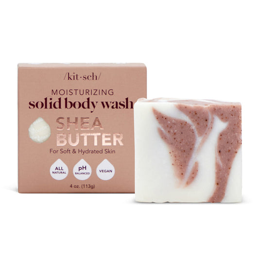 The Kitsch Shea Butter Moisturizing Solid Body Wash stands before its beige packaging, featuring a super-hydrating, all-natural, pH-balanced, vegan formula. The white bar includes brown specks of plant-derived exfoliants to gently moisturize your skin.