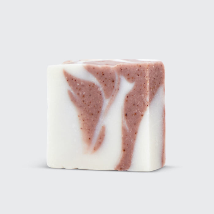 The Kitsch Shea Butter Moisturizing Solid Body Wash is a rectangular soap bar featuring a marbled pattern of cream and reddish-brown on light gray. Infused with plant-derived exfoliants, it offers a smooth texture with darker specks in the reddish areas for gentle, natural cleansing.