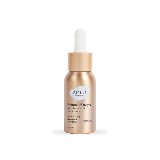 The gold APTO Skincare Shimmer Drops with Turmeric & Niacinamide, Glow Serum bottle features natural, cruelty-free ingredients. Its dropper cap aids in applying this 2 fl oz serum, promising to illuminate, hydrate, and plump your skin.