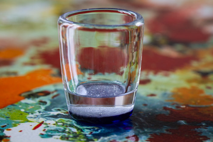 Clear shot glass with a blue-tinted base resting on a colorful abstract surface.