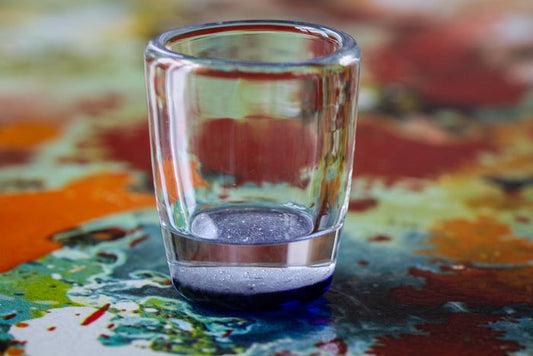 Clear shot glass with a blue-tinted base resting on a colorful abstract surface.
