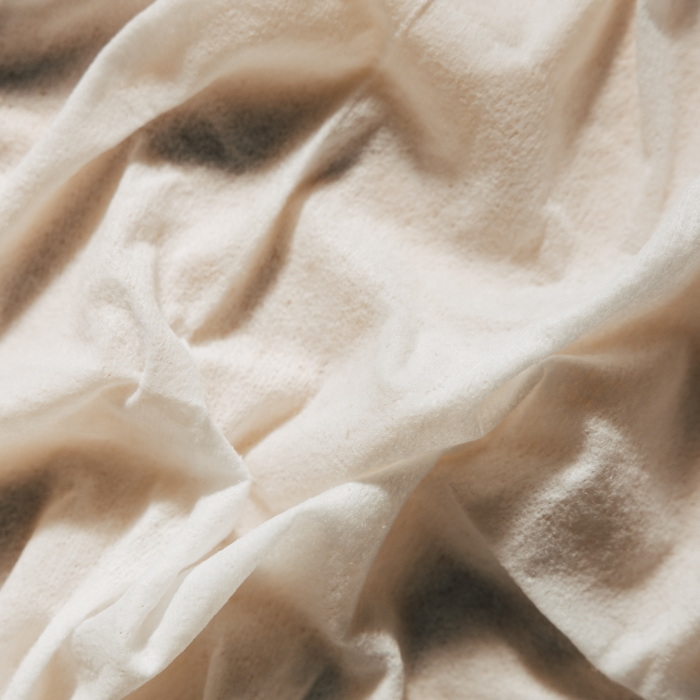 Close-up of YUNI Shower Sheets soft, wrinkled white fabric exhibits gentle shadows and a textured look like cleansing wipes. The material appears soft and smooth, with a slightly creamy hue.
