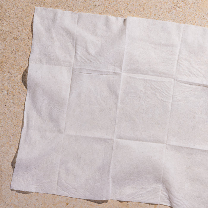 The YUNI Shower Sheets, large and white with a textured grid-like pattern, are laid on a beige background, ideal for on-the-go cleansing.