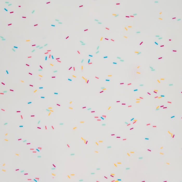 Colorful sprinkles in pink, blue, orange, and yellow are evenly spread on a white background of the eco-friendly GIR Silicone Baking Mat, creating a playful and bright pattern.