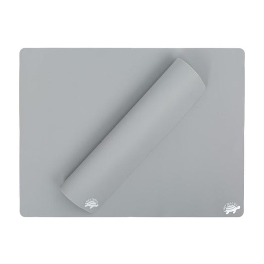 A gray, food-grade silicone baking mat from Net Zero Co.s Reusable Baking Un-Paper collection is laid flat with a corner rolled over. The surface features a small hedgehog logo in the bottom-right corner, providing an eco-friendly alternative to parchment paper.