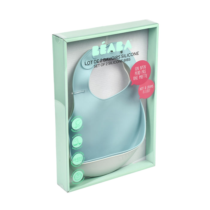 A transparent box holds a pair of green BEABA Silicone Bibs, essential for baby feeding. The packaging highlights easy cleaning and dishwasher-safe features, with text in English and French. Each bib includes a pocket to catch spills.