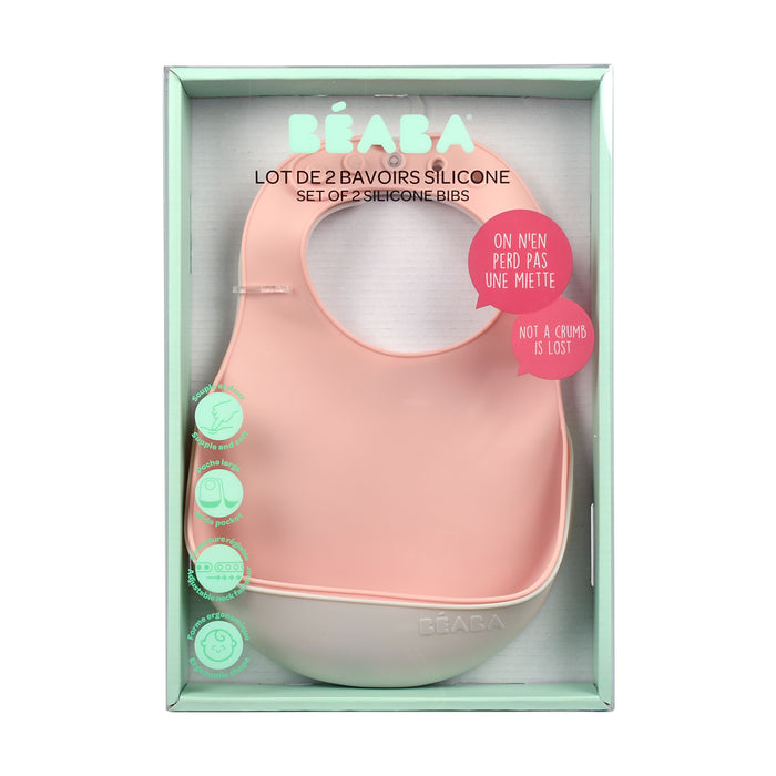 The BEABA Silicone Bibs, a baby feeding essential in soft pink and white, feature a crumb catcher and adjustable design. The packaging displays icons and text in French and English, highlighting their dishwasher-safe material for easy cleaning.