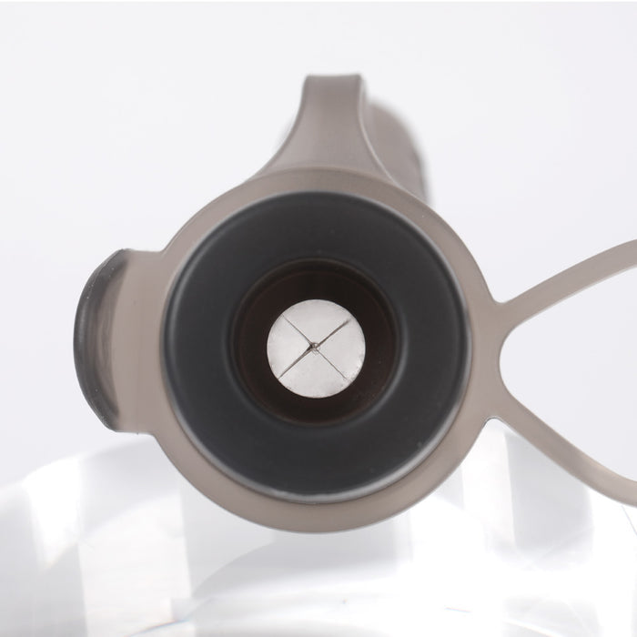 Close-up of the Haakaa Silicone Milk Storage Bag & Sippy Spout Combo Pack lid featuring a beige plastic exterior, black interior, crossed slit opening, and attached carrying loop, ideal for eco-conscious parents. The clear background hints at a reflective surface below.