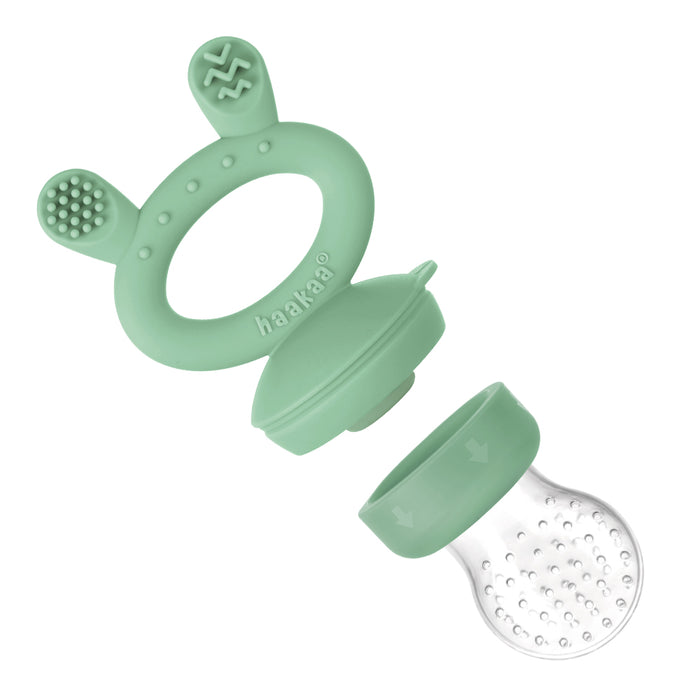 The Haakaa Silicone Freeze-N-Feed Mini Combo is a green silicone baby feeder with textured ears, a round handle displaying the brand name, and a detachable clear silicone pouch with small holes for easy teething relief feeding.