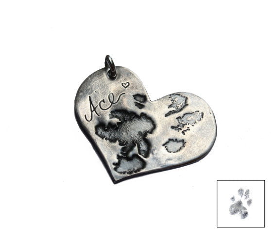 Heart shaped silver nose print and pawprint pendant with a small inset paw print illustration on white background