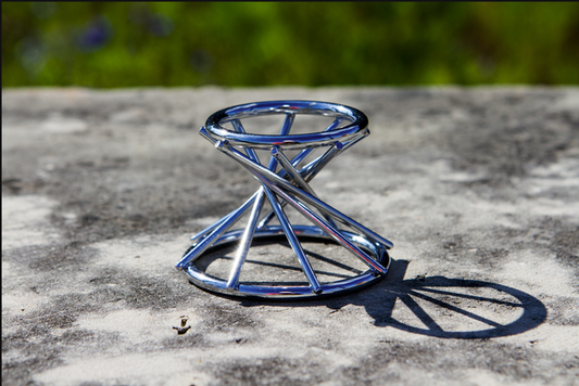 Silver swirl metal stand for 3 inch orb paperweights shown on a textured stone surface outdoors