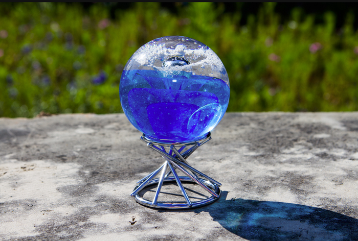 Blue orb displayed in the silver swirl paperweight stand outdoors on a concrete surface