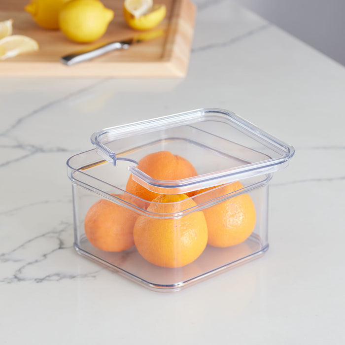 On a marble countertop, iDesigns Single Fridge Bin, crafted from recycled BPA-free plastic, holds four oranges. Nearby, a wooden cutting board with three lemons and a knife is ready for use. This durable container is perfect for fresh produce storage in the refrigerator.