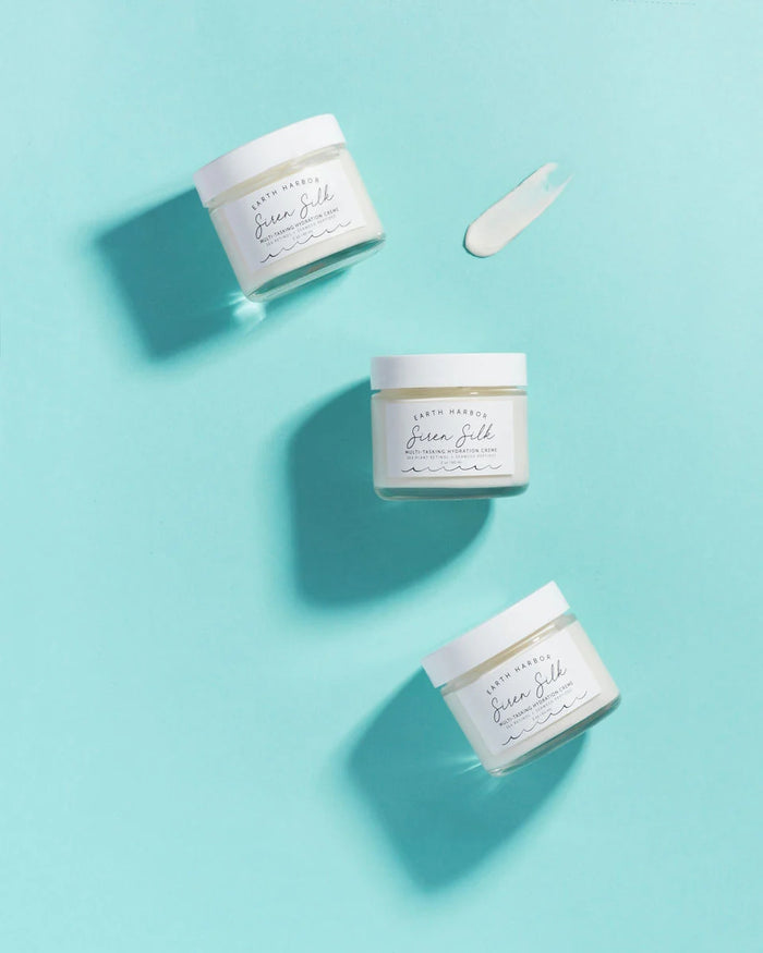 Three jars of SIREN SILK Bio-Retinol Hydration Cream by Earth Harbor sit on a light turquoise background, with one opened to show the bio-retinol-rich cream smeared beside it. Shadows from the jars highlight a minimalist design ideal for anti-aging skincare.