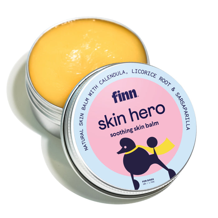 A small tin of Finns Skin Hero - Soothing Skin Balm for Dogs contains a yellow salve with soothing ingredients like calendula, licorice root, and sarsaparilla. The lid displays an abstract dog illustration, perfect for pampering your pets skin.