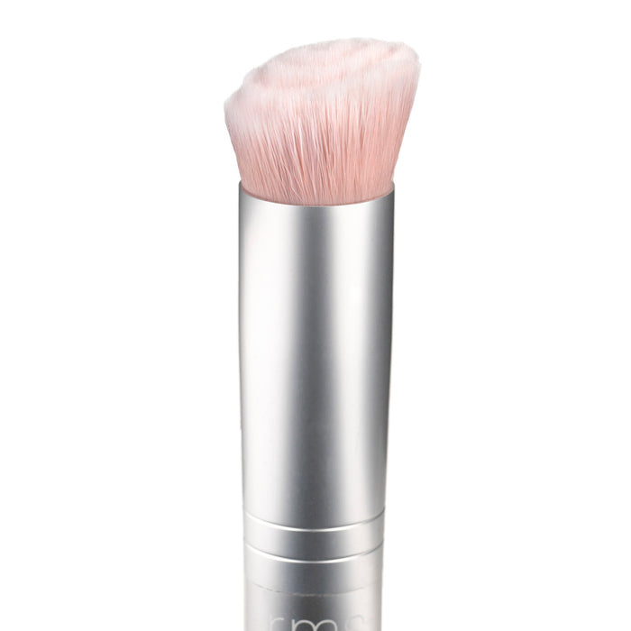 The RMS Beauty Skin2Skin Foundation Brush, featuring dual technology, has a metallic silver handle and soft, densely packed pink bristles tilted at the top, set against a plain white background.