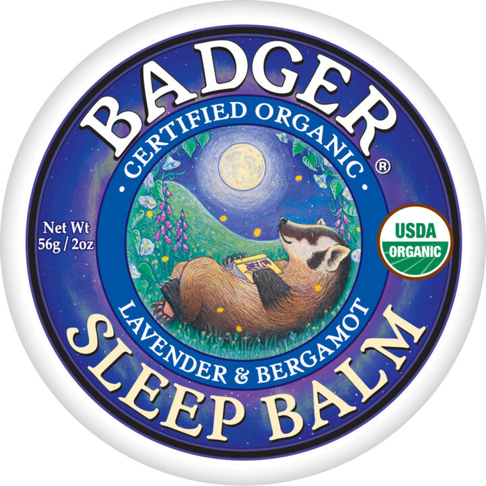 The round tin of Badger Balm Sleep Balm features a serene illustration of a badger resting with a book under the night sky, highlighting its natural sleep remedy benefits with Certified Organic Lavender & Bergamot and a USDA Organic label among the moon and stars.