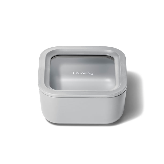 A small, square, light gray food container by Caraway features a snug-fitting ceramic-coated glass lid with Air Release technology, combining a sleek modern design for optimal freshness.