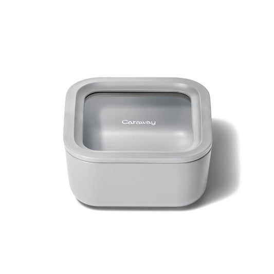 A small, square, light gray food container by Caraway features a snug-fitting ceramic-coated glass lid with Air Release technology, combining a sleek modern design for optimal freshness.