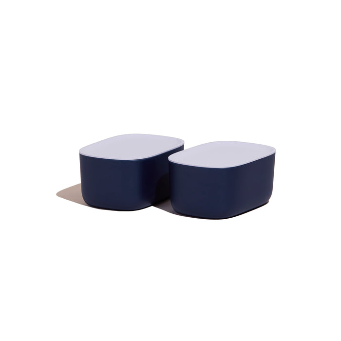 Two sleek, minimalist Small Storage Bins by Open Spaces offer a stylish solution with rounded edges and two-tone design. The dark blue bases contrast beautifully with the white tops, perfect for organizing small items and casting subtle shadows on a plain white background when placed together.