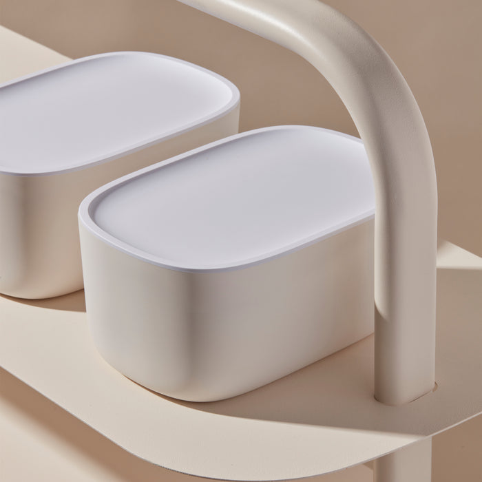 Open Spaces Small Storage Bins, featuring minimalist beige containers with white lids, rest on a light-colored shelf with curved edges. Their sleek design seamlessly blends with neutral tones to stylishly organize small items.