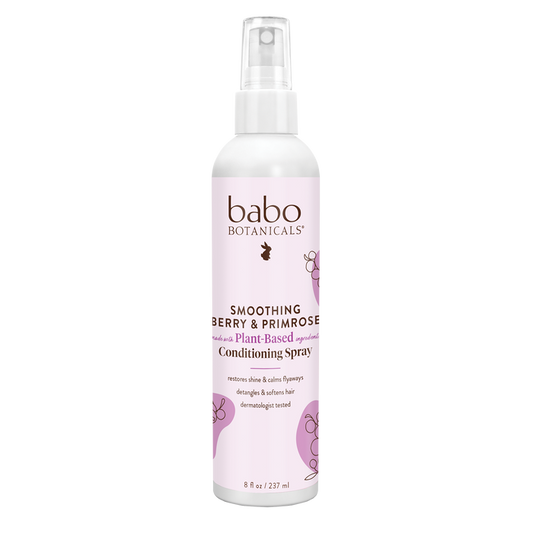 The Babo Botanicals Smoothing Conditioning Spray features a pink label with floral graphics. This silicone-free, plant-based spray tames frizz and nourishes hair for smoothness and shine.