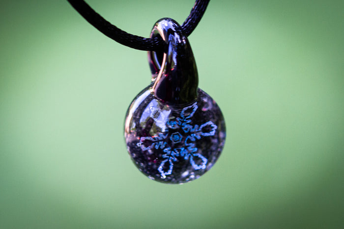 Holographic blue and silver snowflake pendant encased in glass infused with cremation ash, suspended from an adjustable cord.