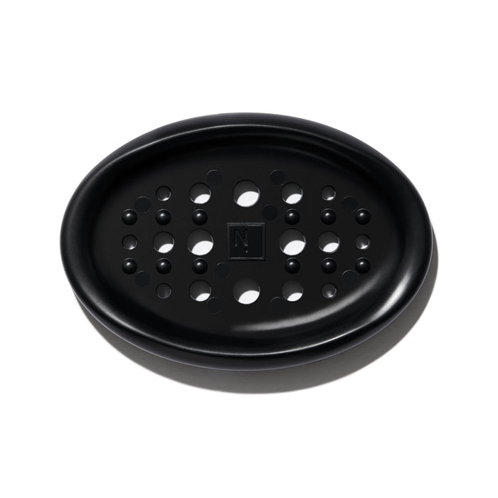 The NOT!CE Hair Co Bar Dish is a black, oval silicone plate with circular drainage holes and a textured N logo, perfect for plastic-free hair care enthusiasts.