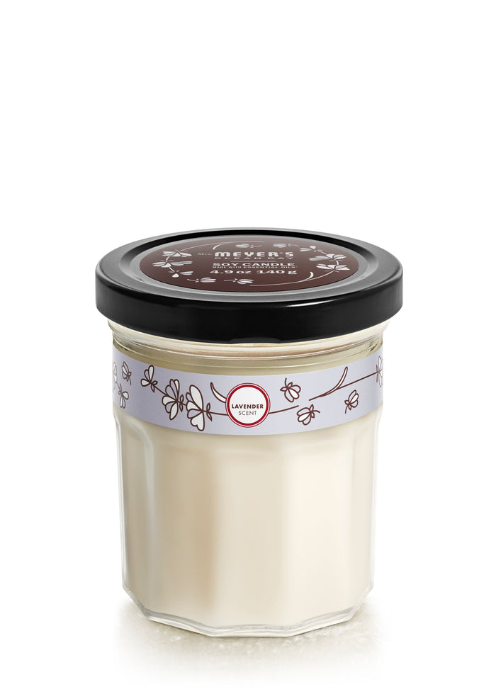 The Mrs. Meyers Soy Glass Jar Candle includes a vegetable soy wax and black lid, with its brown label showcasing floral designs and white text. Lavender illustrations adorn the jars band, and a red label reads LAVENDER. Experience the soothing scent of this cruelty-free candle.