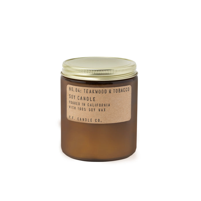 A brown amber jar with a gold lid holds the No. 04: Teakwood & Tobacco Soy Candle by P.F. Candle Co., offering a fresh, earthy scent. Made with 100% soy wax and poured in California, it features an elegant label indicative of its quality craftsmanship.