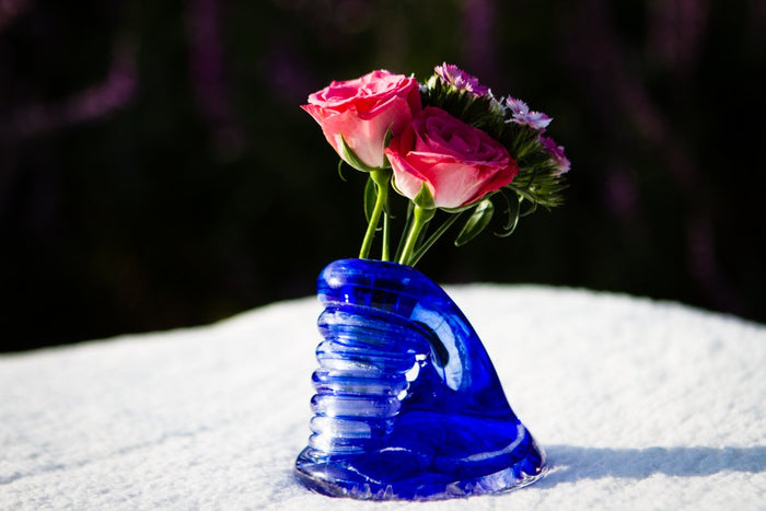 Blue Spiral Bud Vase with cremains holding pink roses and small purple flowers on a snowy surface with a dark backdrop