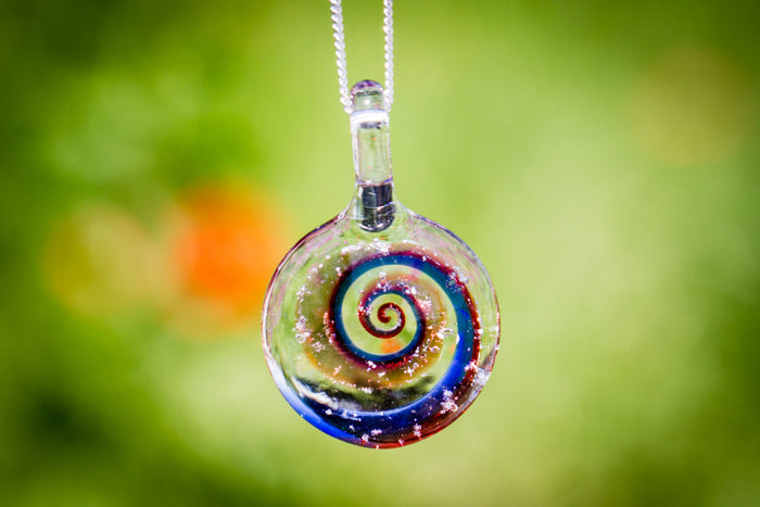 Spiral glass pendant with a vivid multicolor swirl infused with cremation ashes, suspended from a silver chain against a soft green background