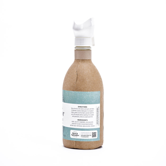 The Root & Splendor Stain Remover features a spray bottle encased in eco-friendly brown paper, with a white plastic nozzle. Its blue and white label details natural ingredients, usage directions, and stain remover properties, along with a small logo and QR code at the bottom.
