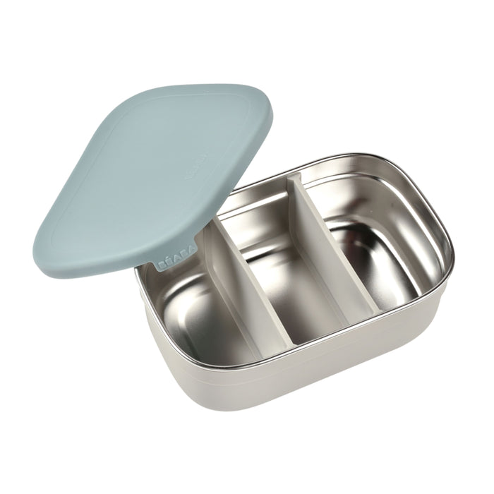 The BEABA Stainless Steel Bento Lunch Box showcases a partially open light blue lid with silicone dividers, revealing its eco-friendly divisions. Its exterior boasts a smooth, light gray finish.