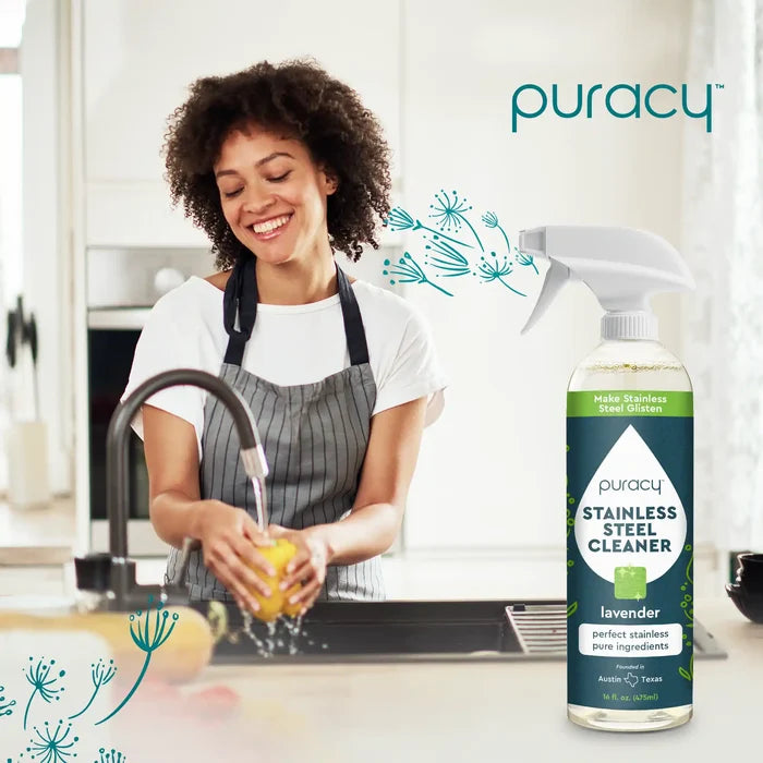 A woman smiles while washing dishes in the kitchen, a bottle of Stainless Steel Surface Cleaner with its plant-based formula catching the light beside her. #common #size_standard