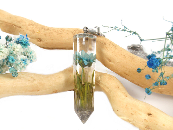 Close up of crystal resin pendant with blue starflower and moss, cremains embedded, attached to a silver chain