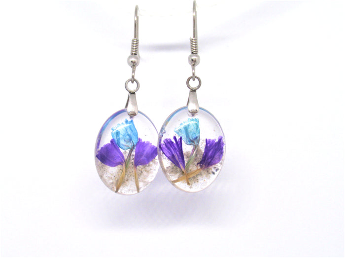 Oval crystal resin earrings containing blue and purple statice flowers with cremains on surgical steel hooks