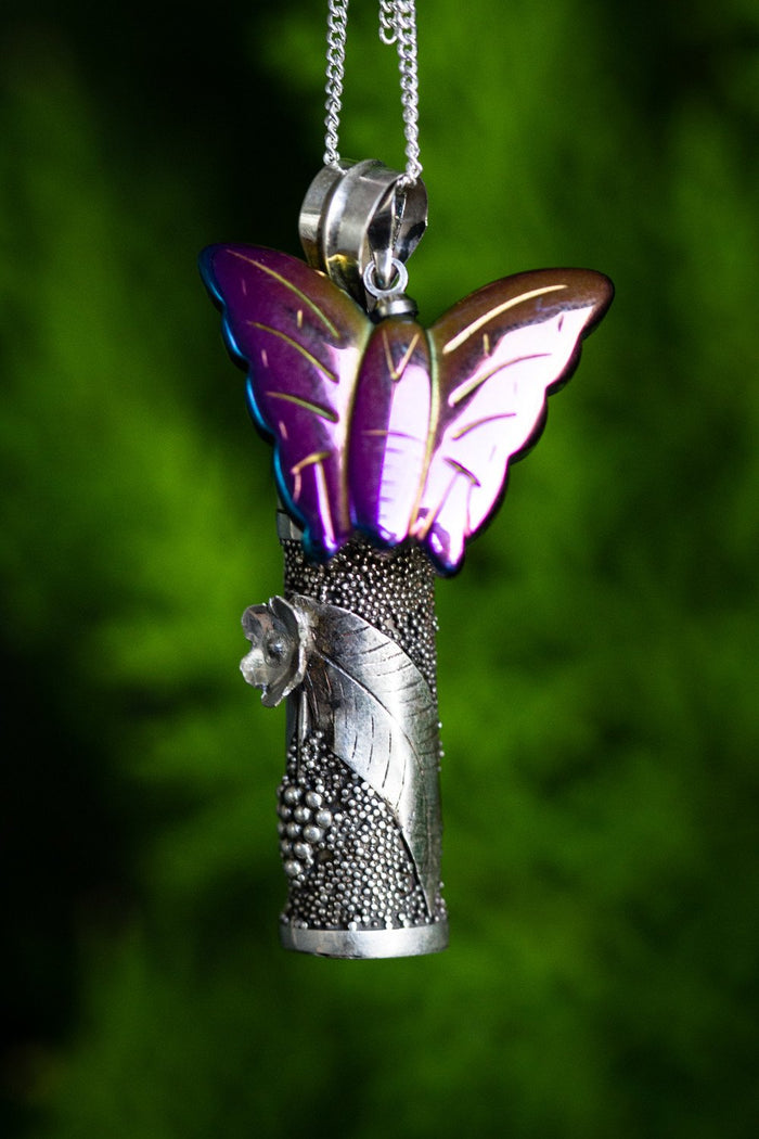 Sterling silver cremation pendant with a purple butterfly charm set above a textured dotted capsule and leaf accent.
